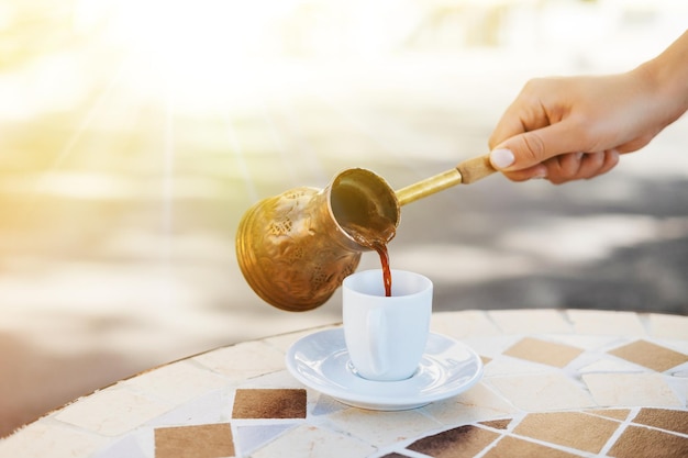 Mão segurando cezve e derramando café turco na xícara