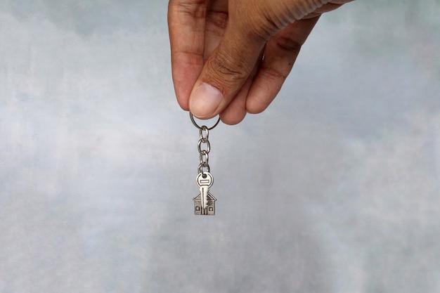 Mão segurando chaveiro em forma de casa e chave com espaço para cópia Conceito de propriedade de casa
