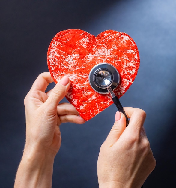 Mão segurando coração vermelho com estetoscópio como símbolo de saúde de caridade e suppo médico cardiológico