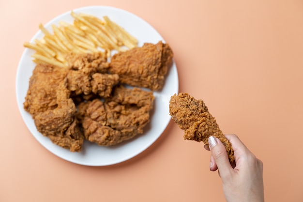 Mão segurando coxinhas, frango frito crocante com batatas fritas em chapa branca em fundo laranja.