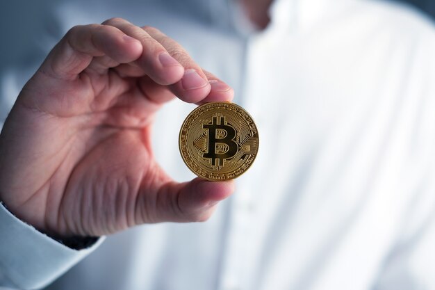 Mão segurando dinheiro virtual Bitcoin dourado.