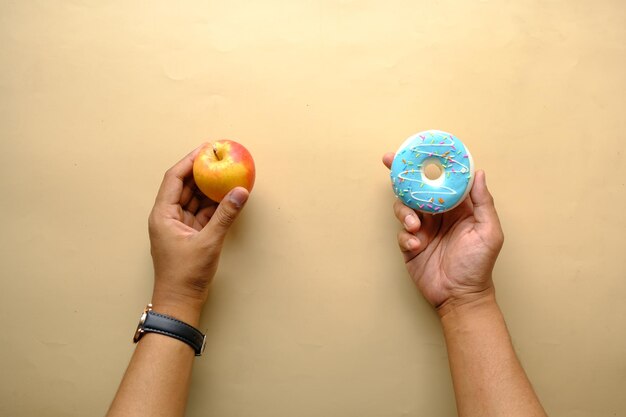 Mão segurando donuts e maçã disponível sobre fundo azul