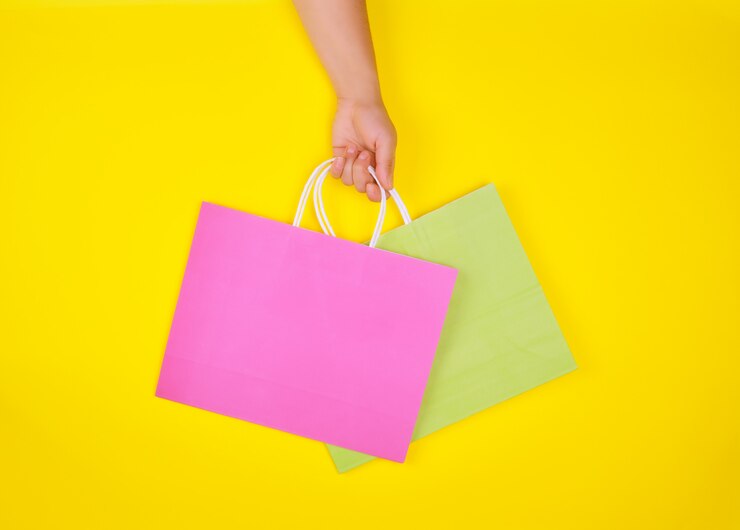 Foto mão segurando duas sacolas de papel em um fundo amarelo