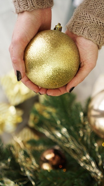 Mão segurando enfeites de bola de ouro no fundo da árvore de Natal