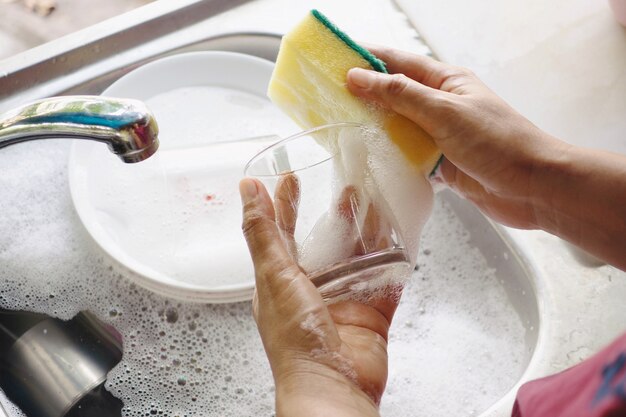 Foto mão segurando esfregão preparado lavando um copo e pratos.