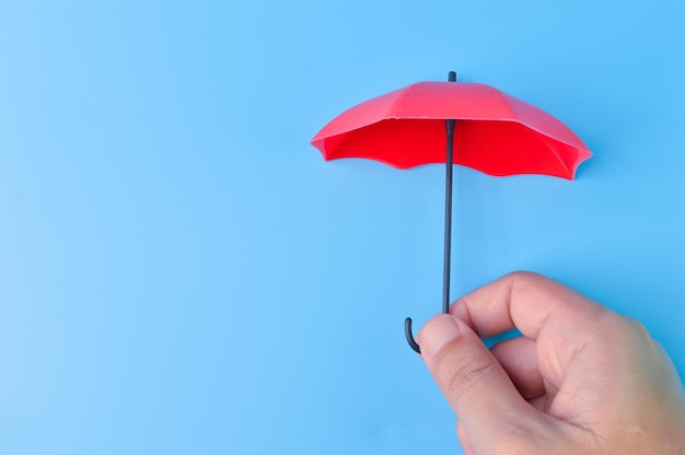 Mão segurando guarda-chuva de brinquedo vermelho isolado em um fundo azul