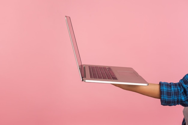 Mão segurando laptop prateado, closeup de gadget de computador contra fundo rosa, conceito de publicidade na internet, busca de emprego online, conexão sem fio wifi grátis. tiro de estúdio interno isolado, copie o espaço