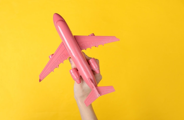 Mão segurando o avião de ar rosa no fundo amarelo Conceito de viagem do minimalismo