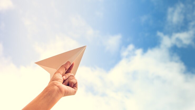 mão segurando o avião de papel no fundo do céu