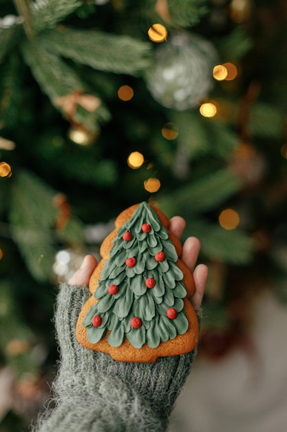 Mão segurando o biscoito de gengibre de árvore de natal no fundo da árvore de natal com luzes Aconchegante casa atmosférica inverno tempo Feliz Natal feriado banner