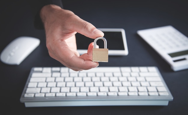 Mão segurando o cadeado. Mesa de trabalho. Internet e segurança do computador