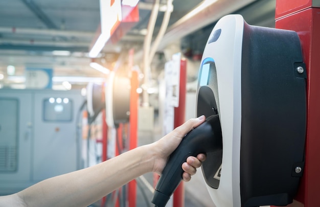 Mão segurando o carregador de plug-in elétrico na estação de carregamento de veículos elétricos Carregamento de carro EV comercial