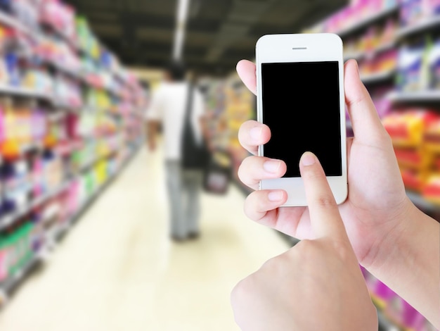 Mão segurando o celular com tela em branco com fundo desfocado de supermercado Conceito de entrega on-line
