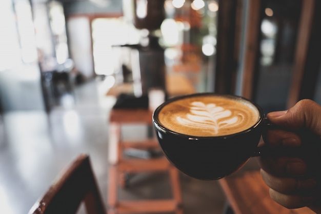 Foto mão segurando o copo de café com leite em desfocar o fundo de café