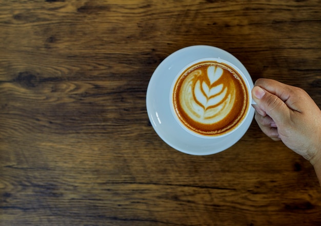 Mão segurando o copo de café na mesa