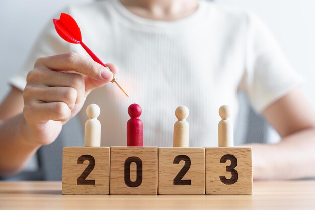 Mão segurando o dardo sobre pessoas vermelhas e blocos de 2023 ano Objetivo plano de ação alvo estratégia liderança Ano Novo e conceito de marketing