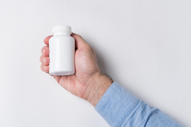 Mão segurando o frasco branco de comprimidos. recipiente farmacêutico, maquete na parede branca
