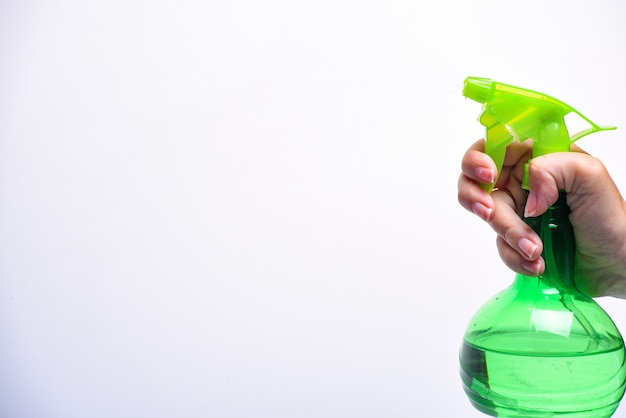 Mão segurando o frasco de spray de plástico verde - segure o frasco de spray de plástico isolado no branco. Homem com pulverizador de água na mão. Copie o espaço