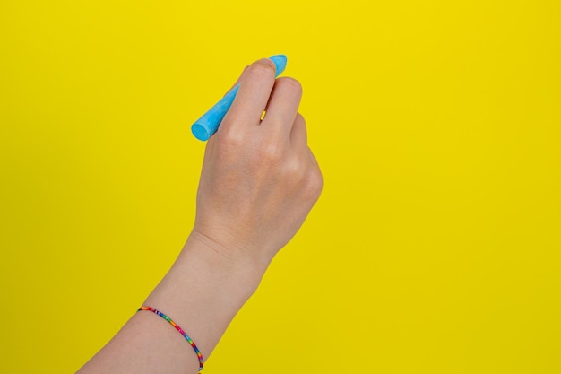 Mão segurando o giz sobre fundo amarelo isolado. Mulher escrevendo algo com giz azul.