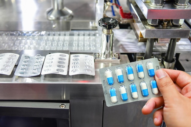 Mão segurando o pacote de cápsulas azuis na linha de produção de comprimidos de remédio Conceito farmacêutico industrial