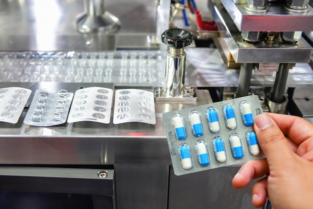 Mão segurando o pacote de cápsulas azuis na linha de produção de comprimidos de remédio Conceito farmacêutico industrial