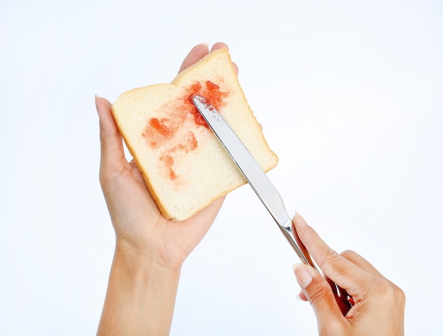 Mão segurando o pão e geléia de morango para o café da manhã no fundo branco