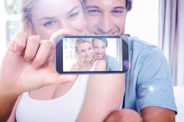 Mão segurando o smartphone mostrando contra um lindo casal jovem relaxando na cama sorrindo para a câmera