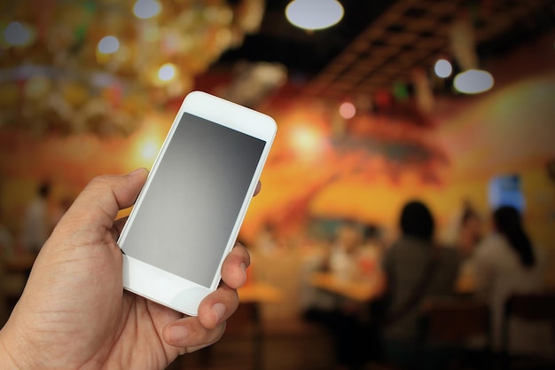 Mão segurando o smartphone no fundo do restaurante desfocado