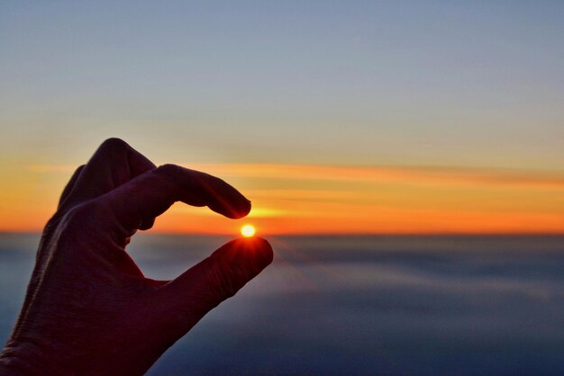 Foto mão segurando o sol sobre o mar durante o pôr do sol