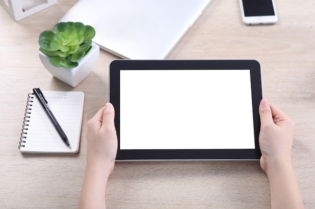 Mão segurando o tablet com smartphone e laptop na mesa de madeira