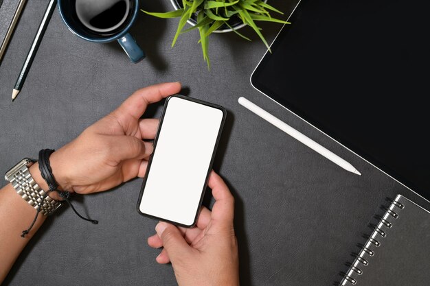 Mão segurando o telefone inteligente moderno com tela em branco isolada para maquete na mesa de escritório