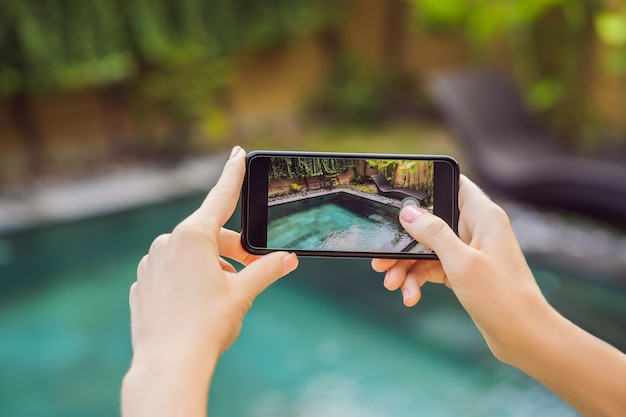 Mão segurando o telefone no fundo da piscina na câmera fotográfica do hotel na tela feche a mão segure o smartphone tire uma foto das férias de verão