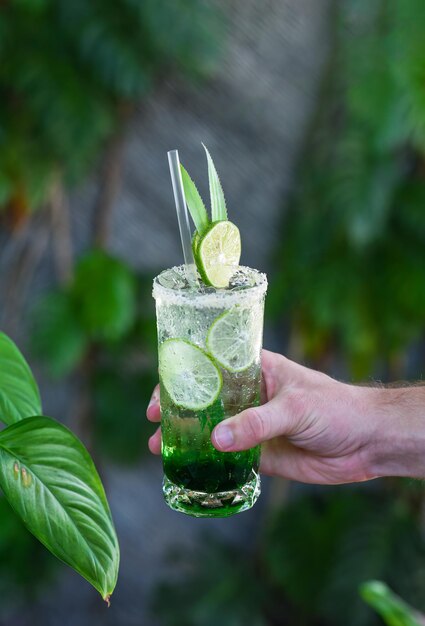 Foto mão segurando panda deixa limonada com coco desidratado e xarope verde em fundo de folhas naturais