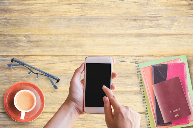 Mão segurando smart phone e notebookpassportglasses e xícara de café na mesa de escritório