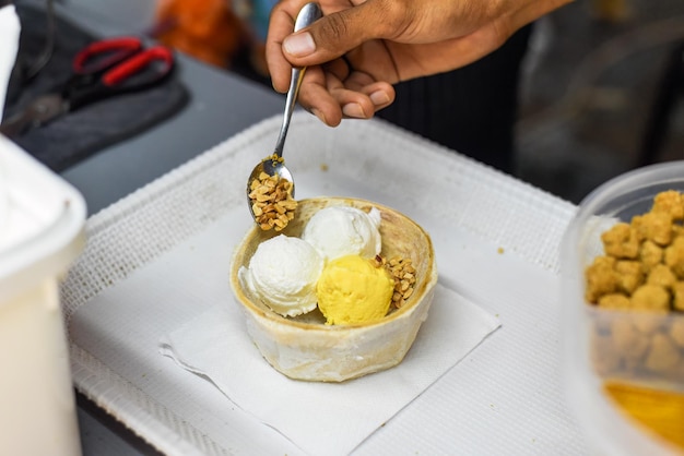 Mão segurando sorvete de coco e manga com casca de coco no mercado de comida de rua Jalan Alor em Kuala