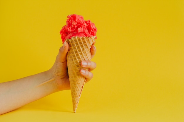 mão segurando sorvete de cone waffle isolado em um amarelo vibrante, cópia espaço