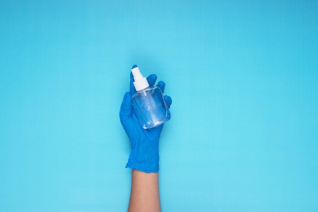 Mão segurando spray desinfetante com luvas médicas azuis sobre fundo azul claro