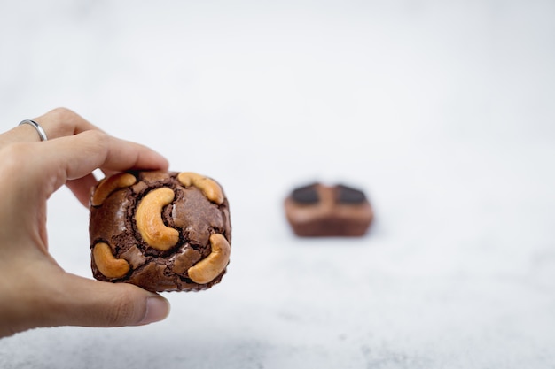 Mão segurando um bolo de brownies no fundo branco para o conceito de padaria, comida e alimentação