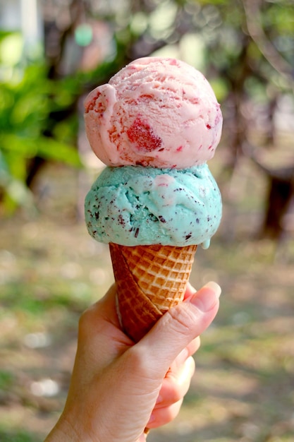 Mão segurando um cone crocante com duas bolas de sorvete contra o jardim de verão embaçado