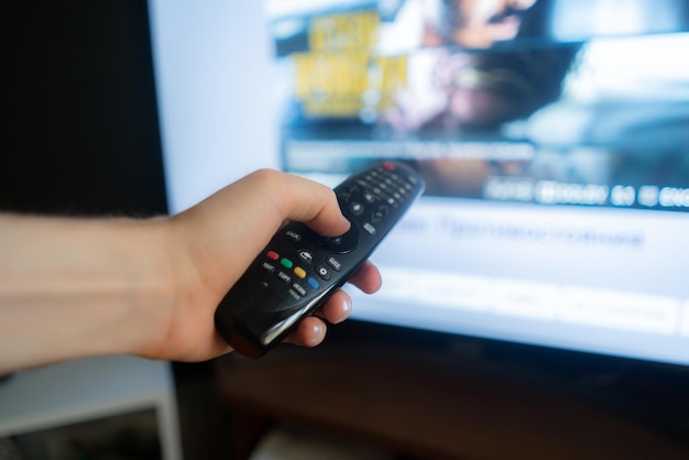 Mão segurando um controle remoto de tv alternando telas de canais de mídia