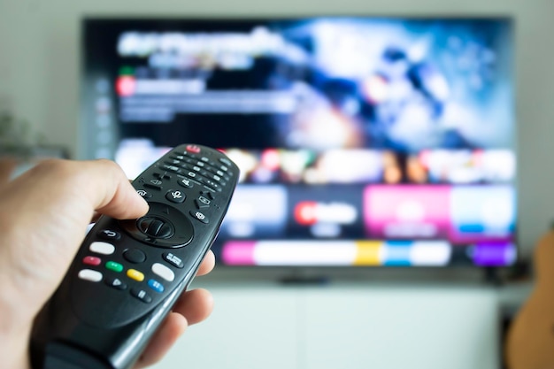 Mão segurando um controle remoto para navegar em programas de TV ou séries