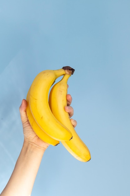 Mão segurando um galho de banana contra o estilo de vida saudável de fundo azul