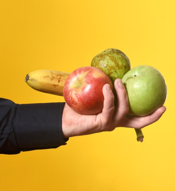 Mão segurando um grupo de frutas em fundo amarelo