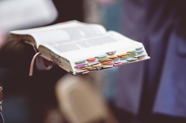 Mão segurando um livro bíblico aberto com marcadores