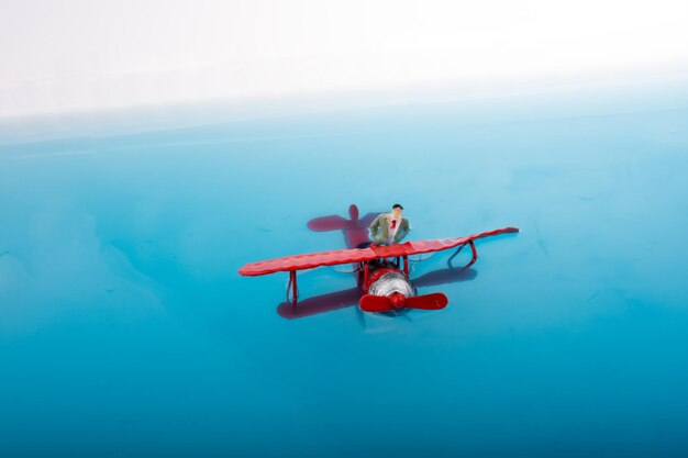 Mão segurando um modelo de avião e uma estatueta de homem em água azul