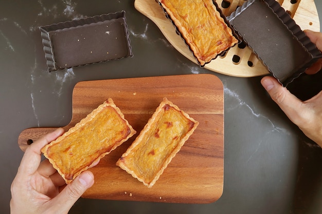 Mão segurando um molde de torta e tortinha de abóbora assada fresca colocando na tábua de pão de madeira