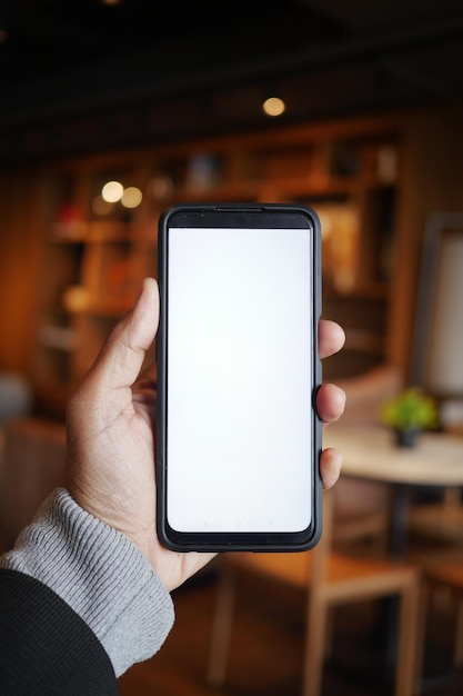 Mão segurando um smartphone em um ambiente aconchegante de café interior