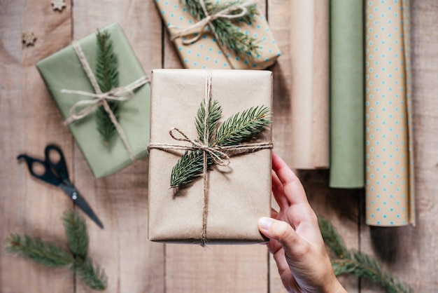 Mão segurando uma caixa de presente ecológica elegante embrulhada em papel artesanal e decorada com galho de árvore de abeto