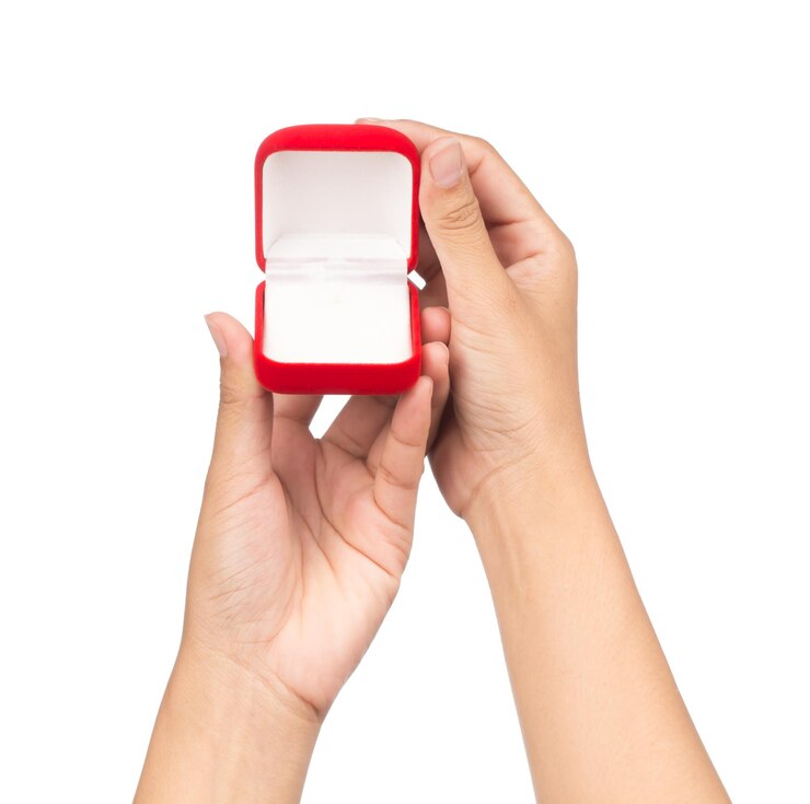 Foto mão segurando uma caixa de veludo vermelho para o anel isolado em um fundo branco.