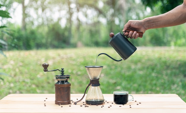 Mão segurando uma chaleira e despejando água quente para fazer café